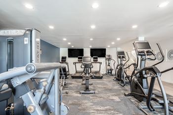A gym with a variety of exercise equipment including treadmills, stationary bikes, and weight machines